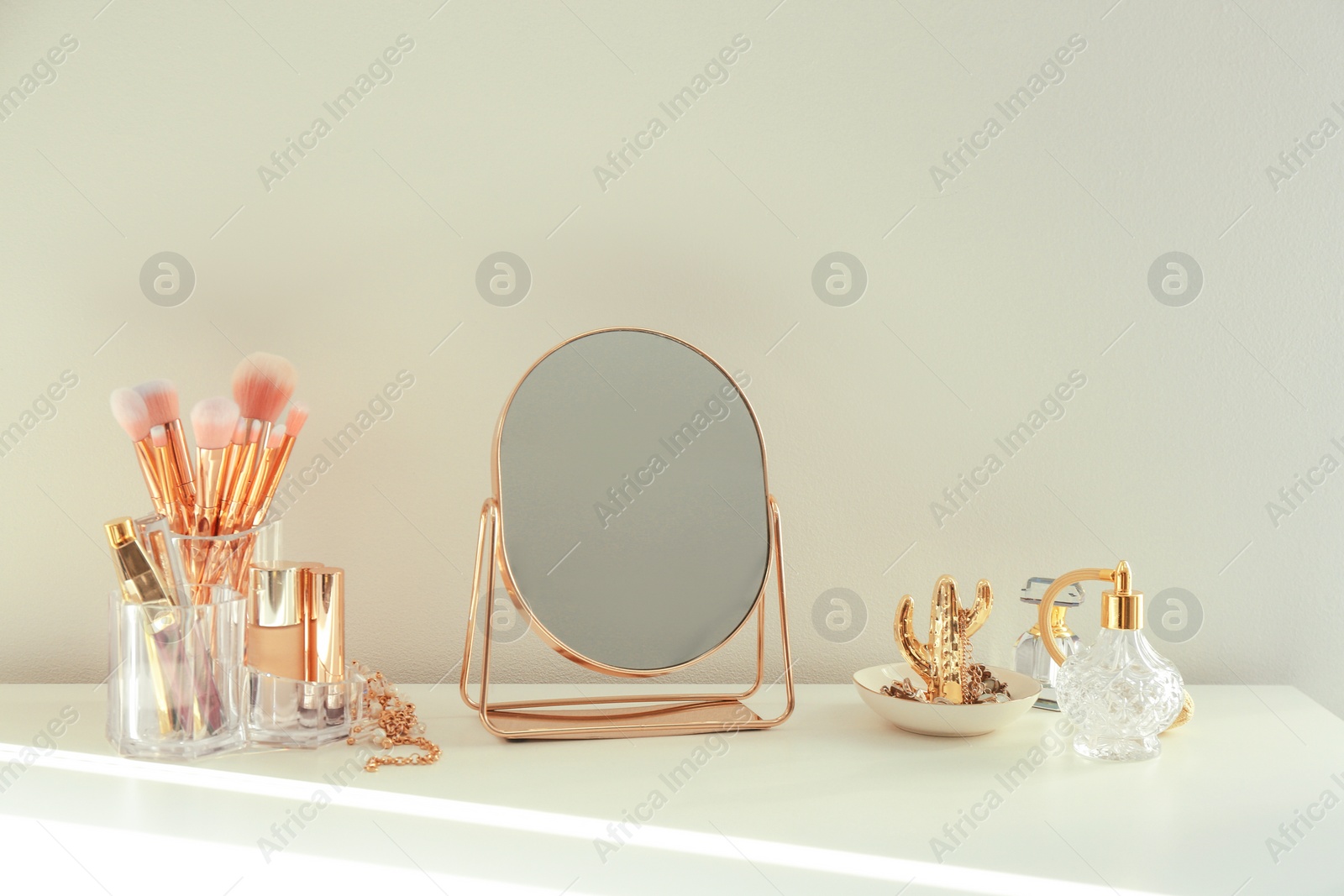 Photo of Small mirror and makeup products on white dressing table indoors