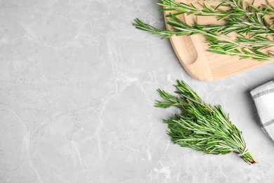 Board with fresh green rosemary on grey marble table, flat lay. Space for text