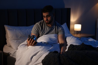 Photo of Sleepy man looking at alarm clock in bed