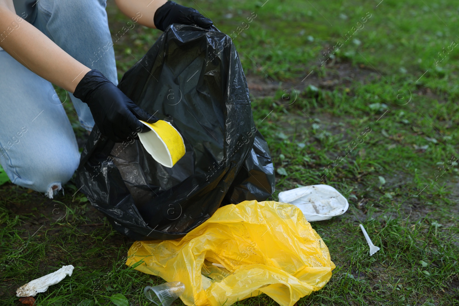 Photo of Woman with plastic bag collecting garbage on green grass, closeup