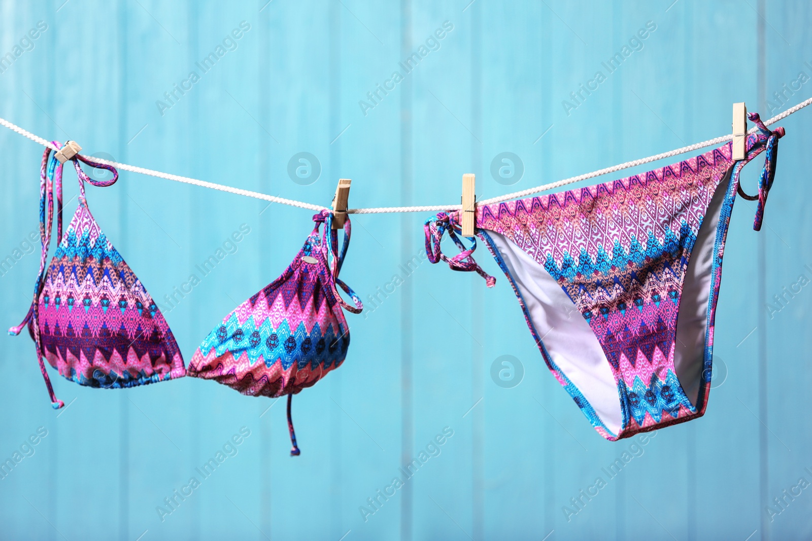 Photo of Stylish bikini hanging on rope against color background