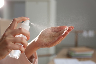 Photo of Woman spraying antiseptic onto hand indoors, closeup