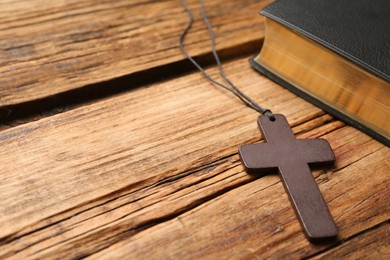 Christian cross and Bible on wooden table, space for text