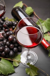 Glass and bottle of red wine and fresh ripe juicy grapes on table