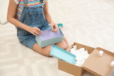Photo of Young woman opening parcel on floor at home, closeup