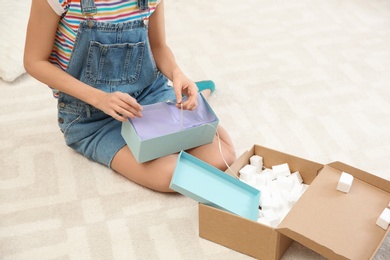 Young woman opening parcel on floor at home, closeup