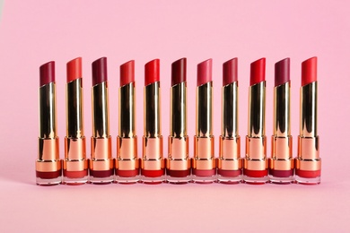 Photo of Set of bright lipsticks in gold tubes on pink background