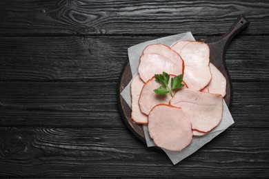 Photo of Delicious cut ham with parsley on black wooden table, top view. Space for text