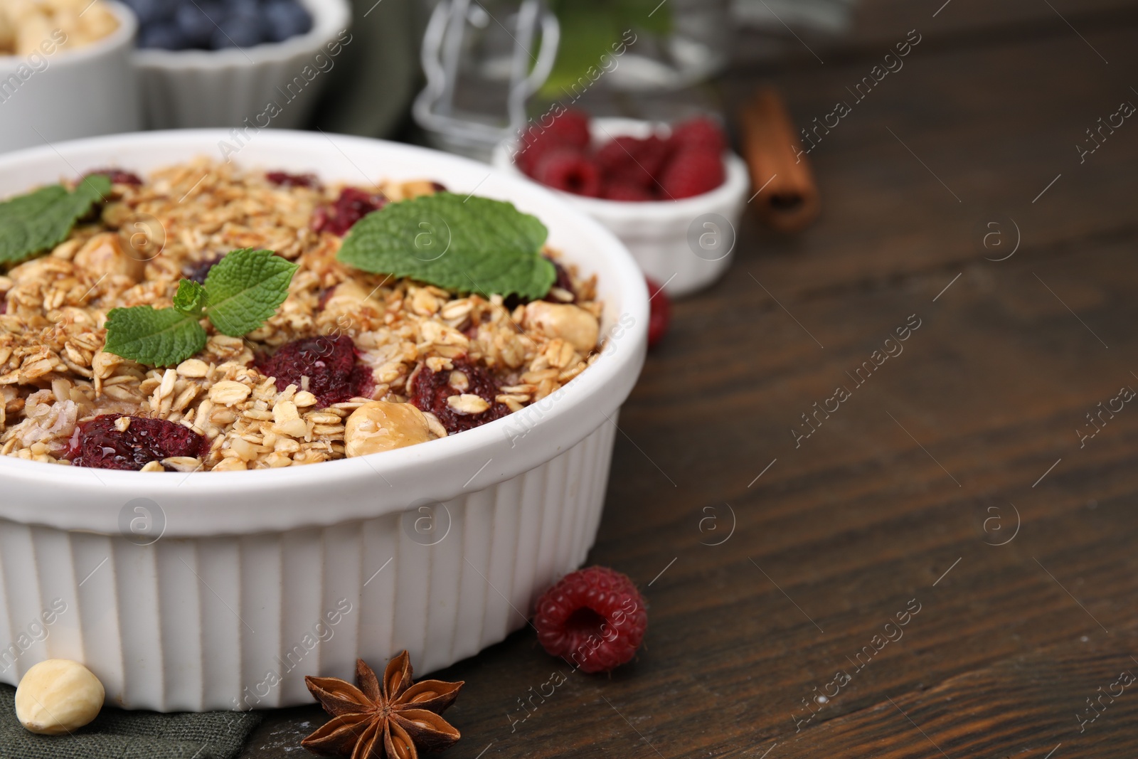 Photo of Tasty baked oatmeal with berries and nuts in bowl on wooden table, closeup. Space for text