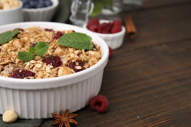 Tasty baked oatmeal with berries and nuts in bowl on wooden table, closeup. Space for text