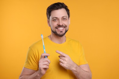 Photo of Happy man holding plastic toothbrush on yellow background. Mouth hygiene