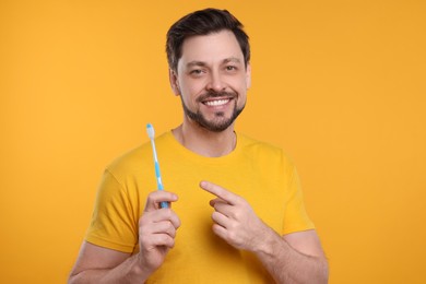 Happy man holding plastic toothbrush on yellow background. Mouth hygiene