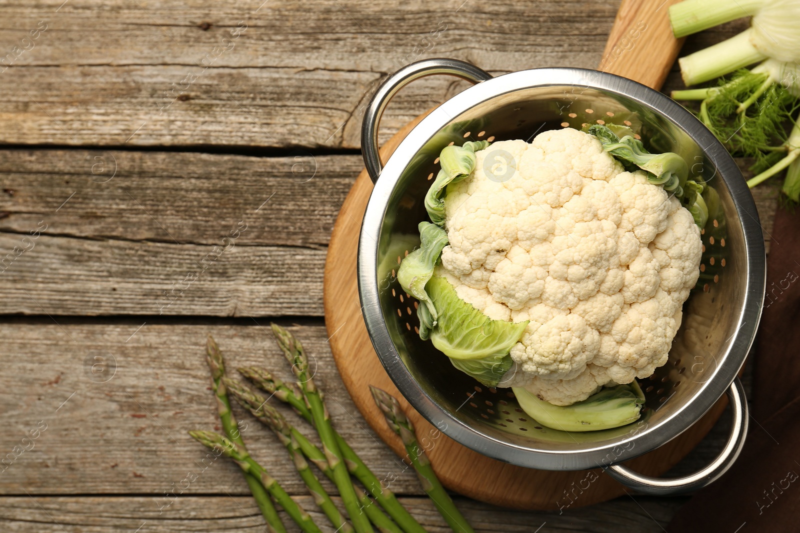 Photo of Metal colander with cauliflower, fennel and asparagus on wooden table, flat lay. Space for text