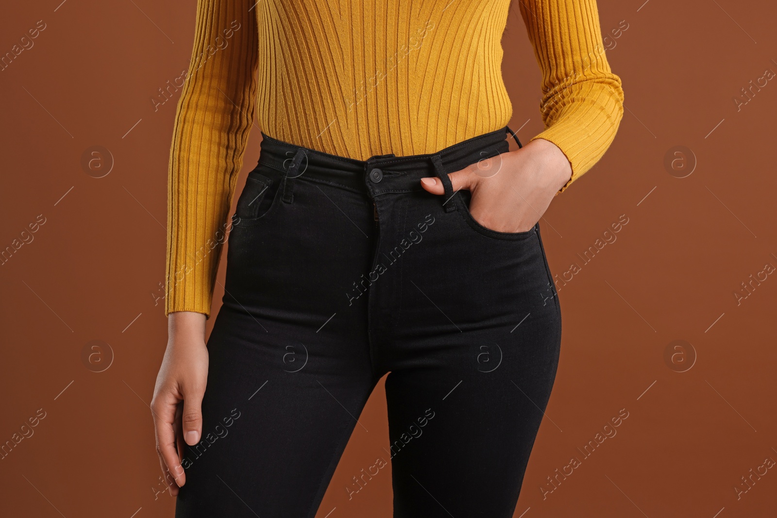 Photo of Woman wearing stylish black jeans on brown background, closeup