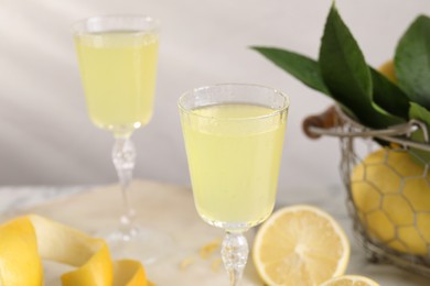 Tasty limoncello liqueur, lemons and green leaves on table, closeup. Space for text