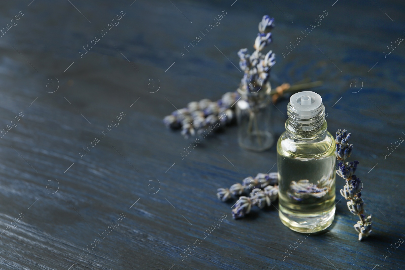 Photo of Bottle of natural essential oil and lavender flowers on blue wooden background. Space for text