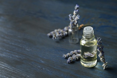 Bottle of natural essential oil and lavender flowers on blue wooden background. Space for text