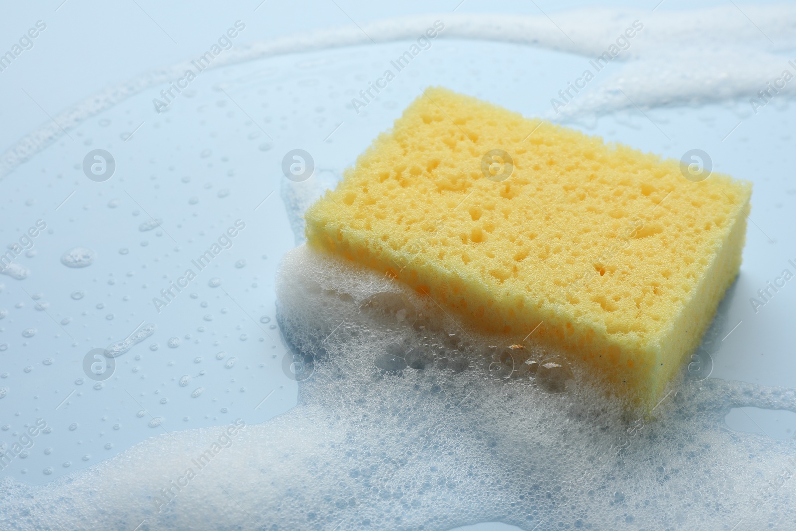 Photo of Yellow sponge with foam on light blue background, closeup