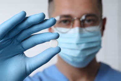 Photo of Doctor holding pill on light background, selective focus. Space for text