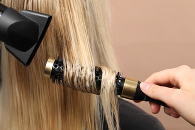 Photo of Hairdresser blow drying client's hair on beige background, closeup