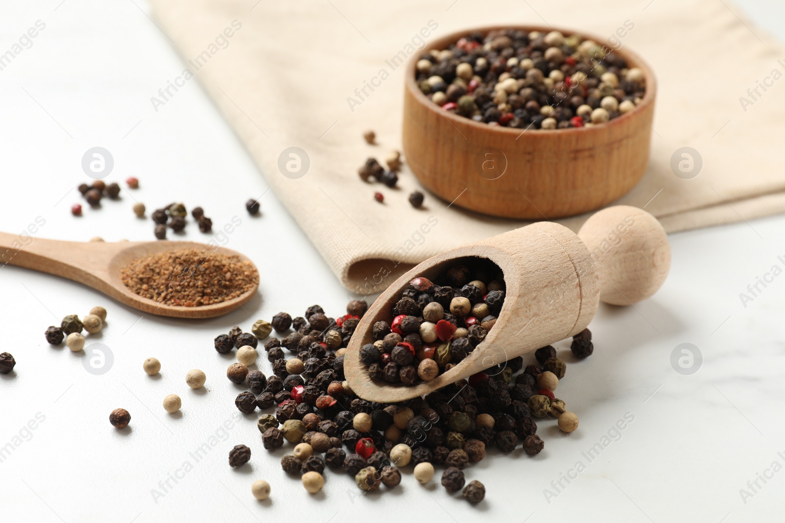 Photo of Aromatic spice. Different peppers in bowl, scoop and spoon on white table, closeup