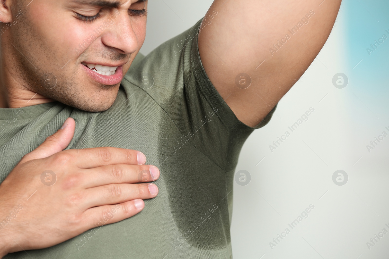 Photo of Young man with sweat stain on his clothes against blurred background, closeup. Using deodorant