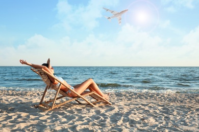 Image of Young woman relaxing in deck chair on beach under sky with flying airplane. Summer vacation