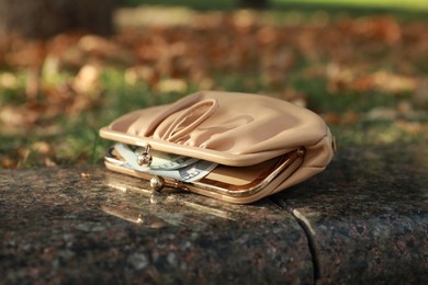 Photo of Beige leather purse on stone curb, closeup. Lost and found