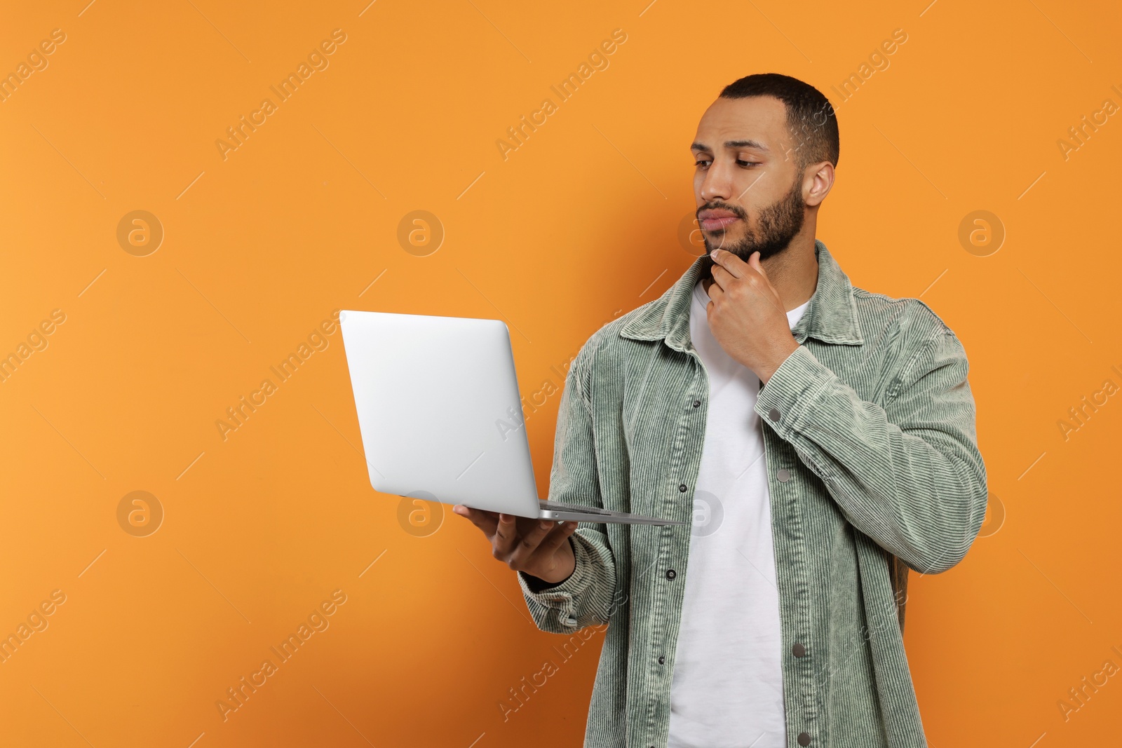 Photo of Thoughtful young man with laptop on orange background, space for text