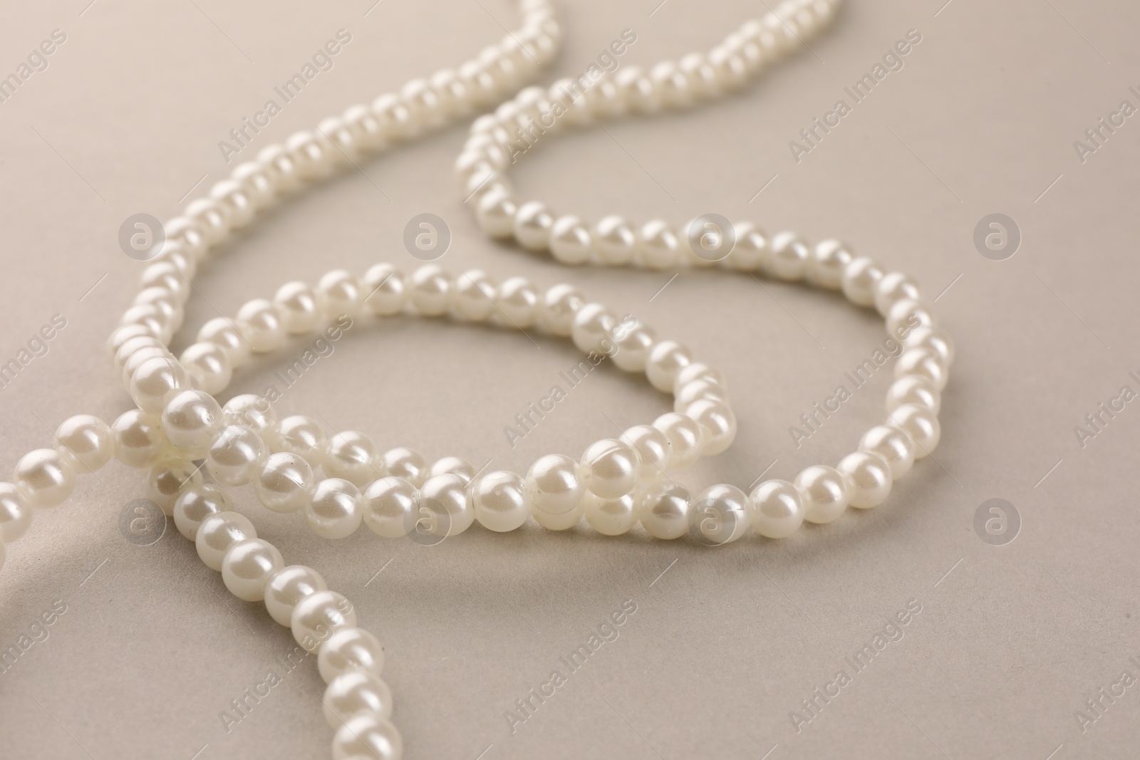 Photo of Elegant pearl necklace on beige background, closeup