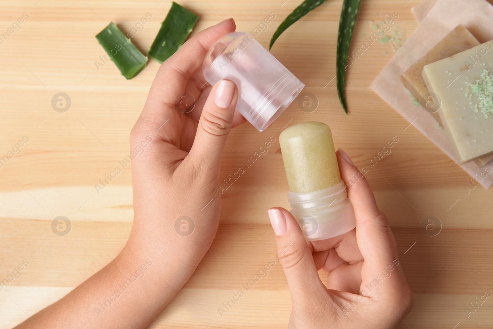 Photo of Young woman holding natural crystal alum deodorant at wooden table, top view