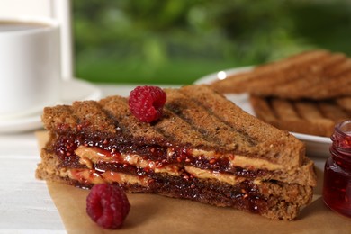 Tasty sandwich with raspberry jam and peanut butter for breakfast on table, closeup