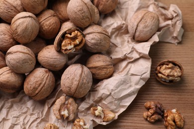 Tasty walnuts and parchment paper on wooden table, closeup
