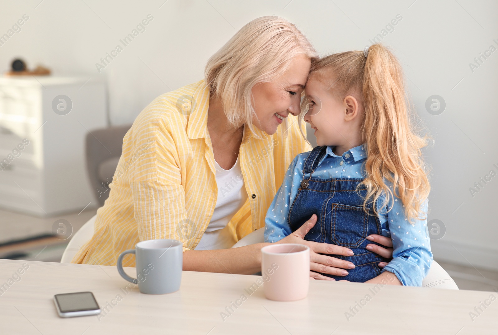 Photo of Portrait of mature woman and her granddaughter drinking tea at table indoors