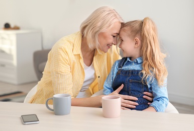 Photo of Portrait of mature woman and her granddaughter drinking tea at table indoors