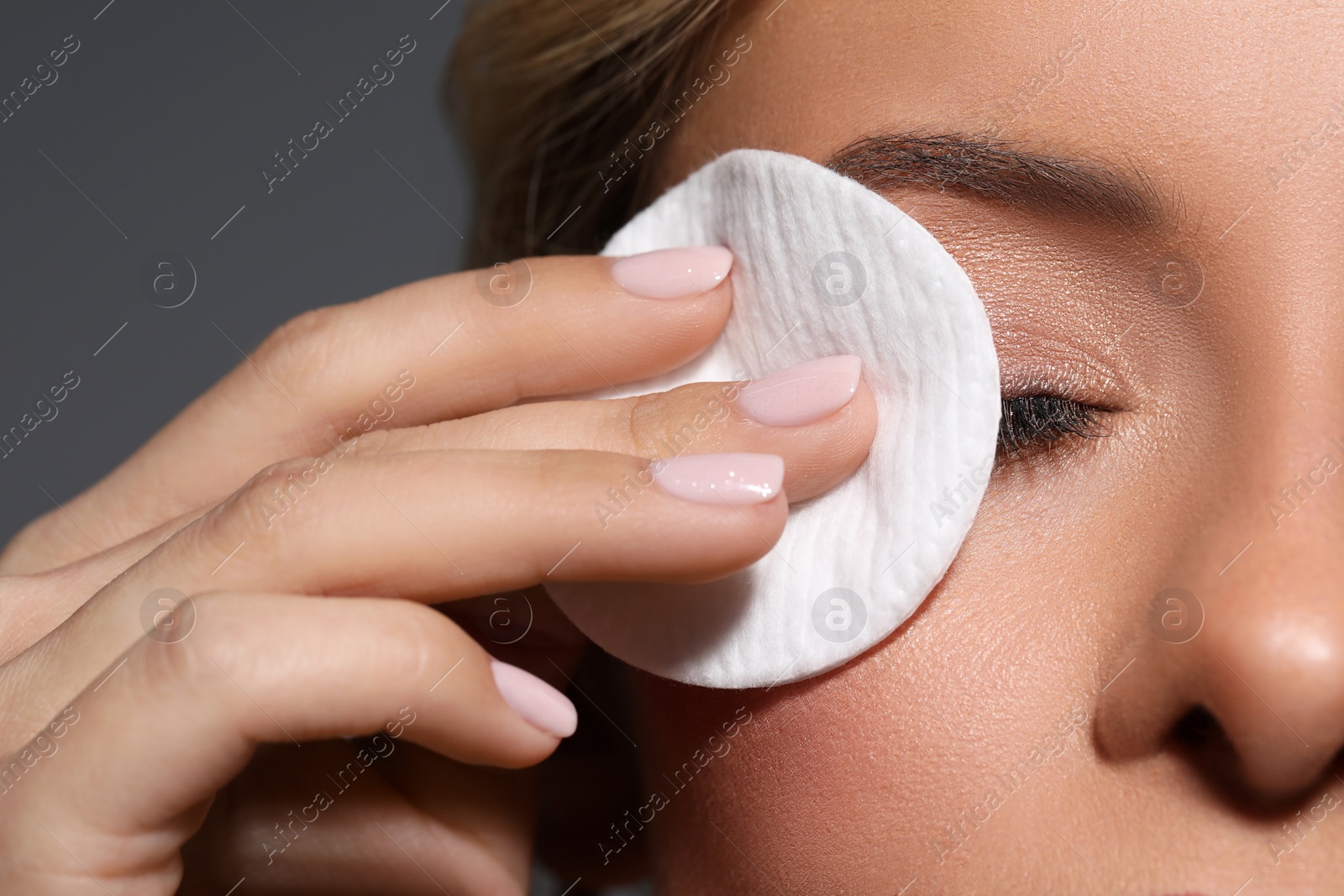 Photo of Beautiful woman removing makeup with cotton pad on dark grey background, closeup