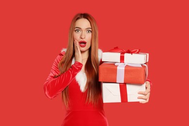 Emotional young woman with Christmas gifts on red background