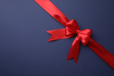 Photo of Red satin ribbon with bow on blue background, top view. Space for text