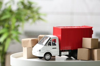 Photo of Toy truck and cardboard boxes on table against blurred background. Courier service