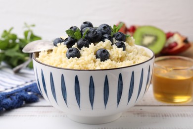Photo of Bowl of tasty couscous with blueberries and mint on white table, closeup