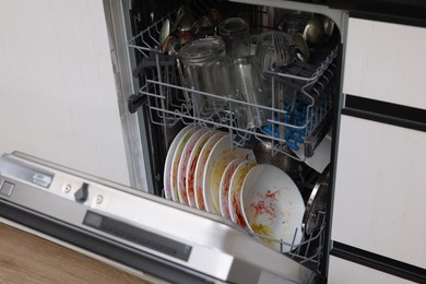 Photo of Open modern dishwasher with dirty tableware in kitchen