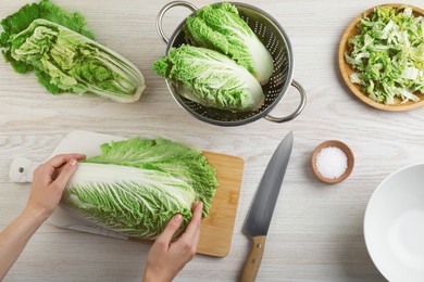 Woman holding fresh ripe Chinese cabbage at white wooden table, top view