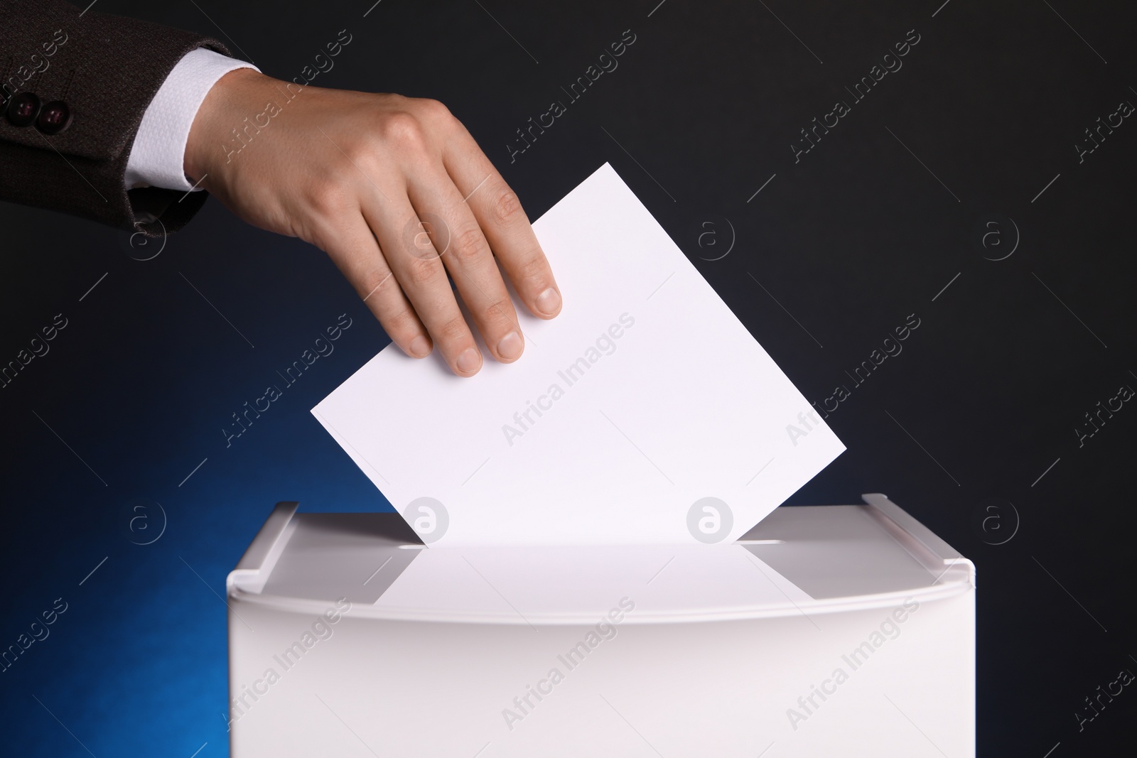 Photo of Man putting his vote into ballot box on dark blue background, closeup