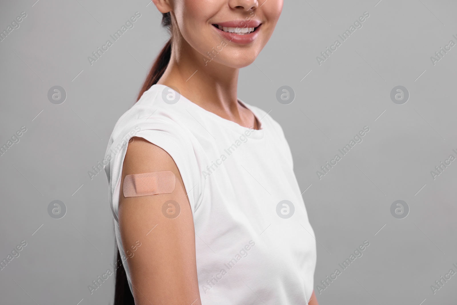 Photo of Woman with sticking plaster on arm after vaccination against light grey background, closeup