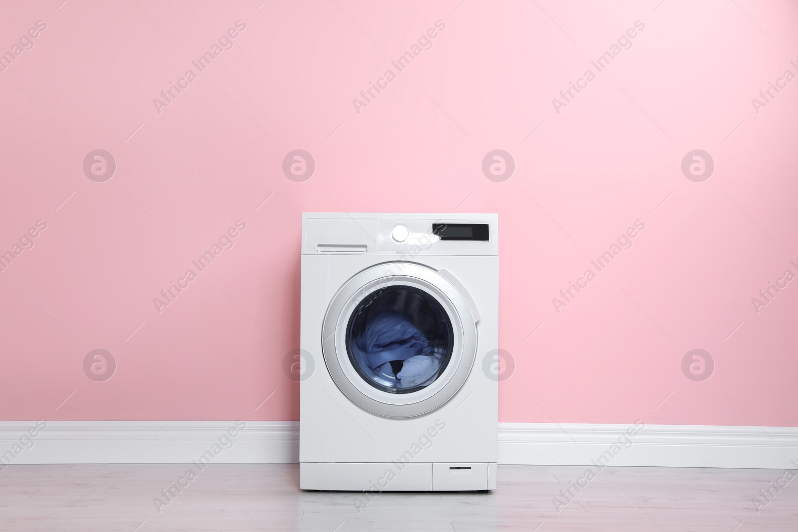 Photo of Washing machine with laundry near color wall. Space for text