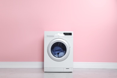 Photo of Washing machine with laundry near color wall. Space for text
