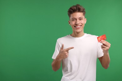Photo of Happy man pointing at credit card on green background. Space for text