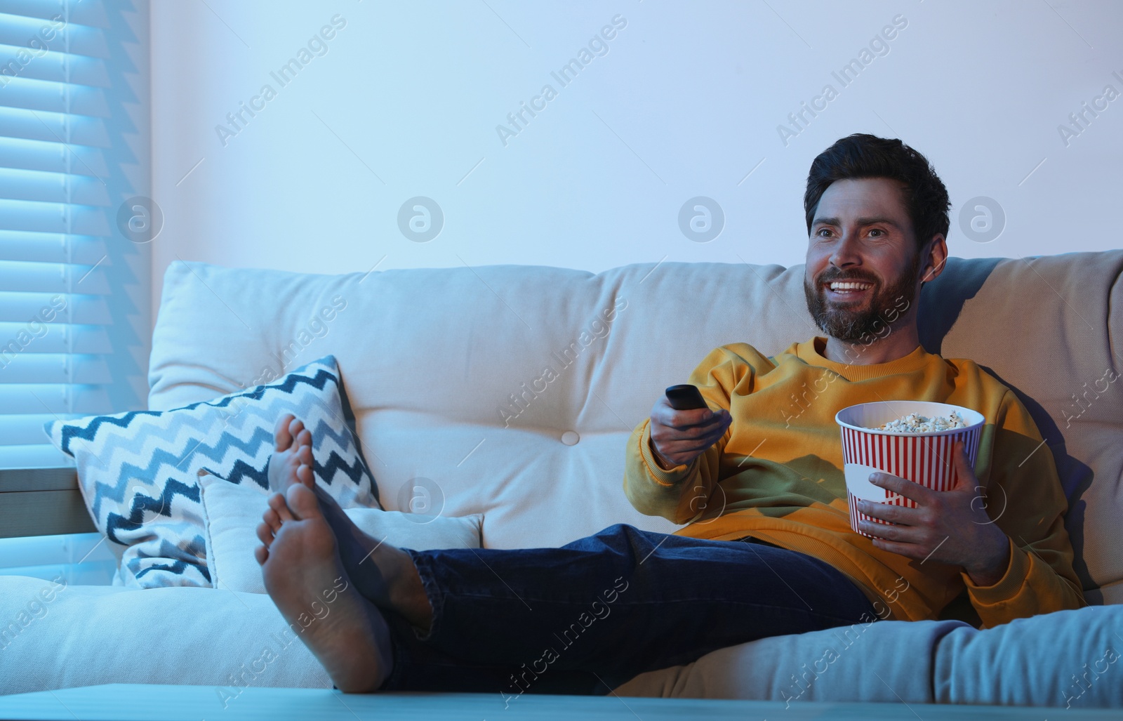 Photo of Happy man watching TV with popcorn on sofa indoors