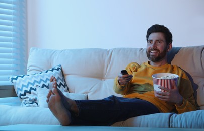 Happy man watching TV with popcorn on sofa indoors
