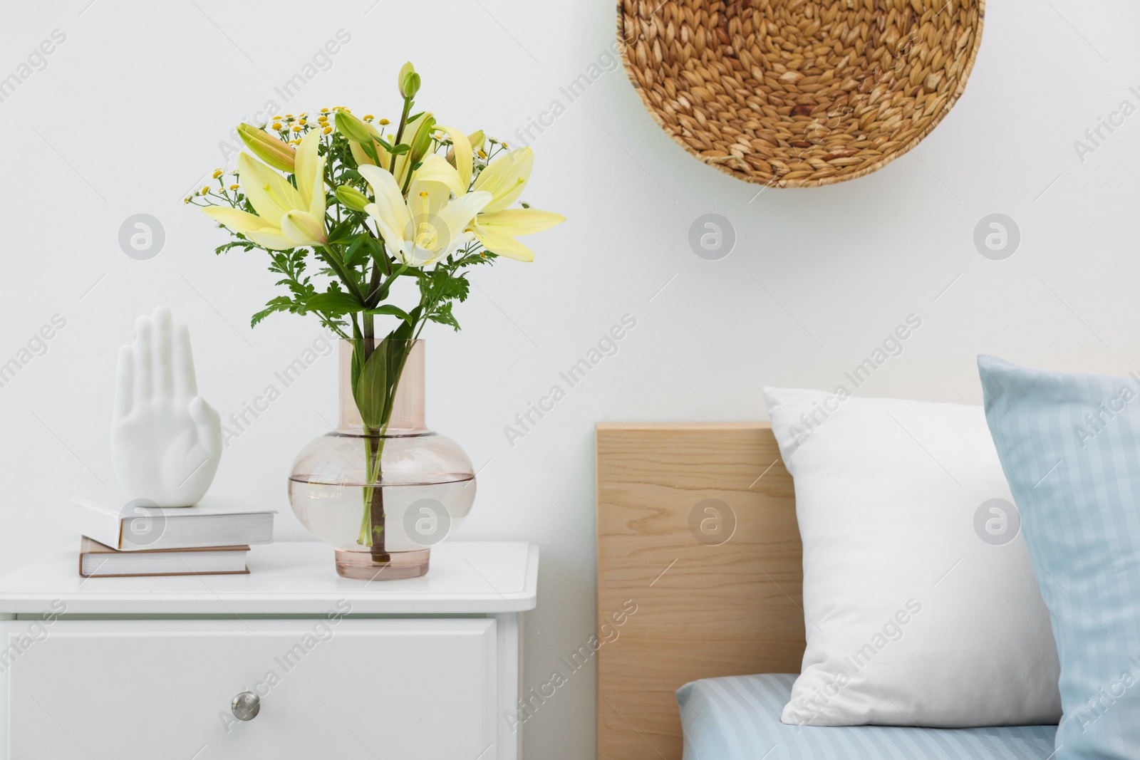 Photo of Vase with bouquet of fresh flowers on nightstand in bedroom